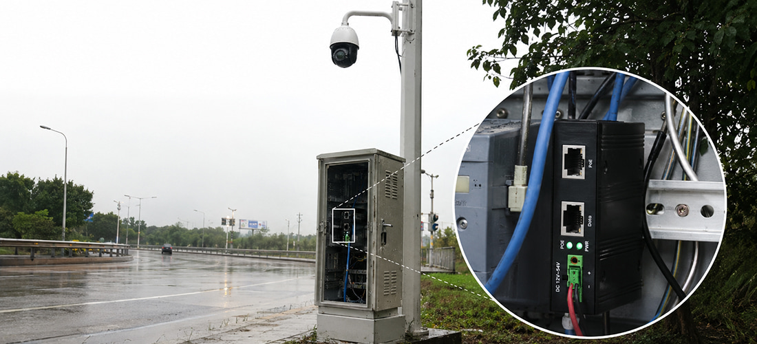 Real-world highway roadside field deployment of Benchu Group industrial PoE++ injector inside an open metal telecommunication cabinet powering a high-draw outdoor PTZ surveillance camera on a pole during wet rainy weather conditions.